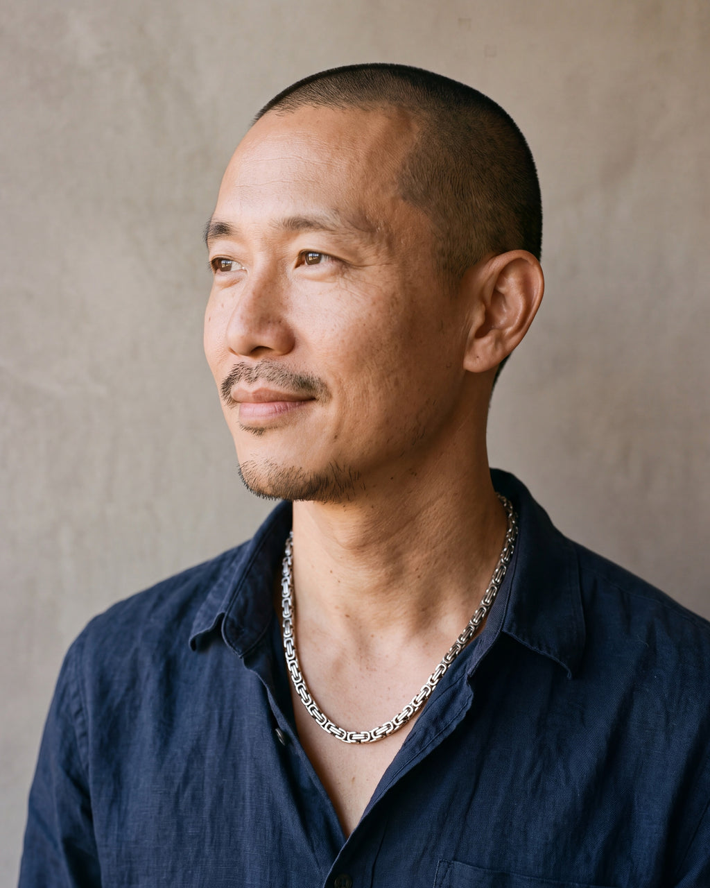 Man in a navy linen shirt by a window wearing the silver Atlas Byzantine chain