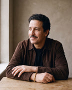 Man in a brown suede overshirt seated at a wooden table, wearing the gold-tone Atlas Byzantine link bracelet