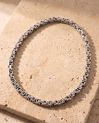 The whole silver-tone Atlas Byzantine chain laid on warm stone, lobster clasp closed