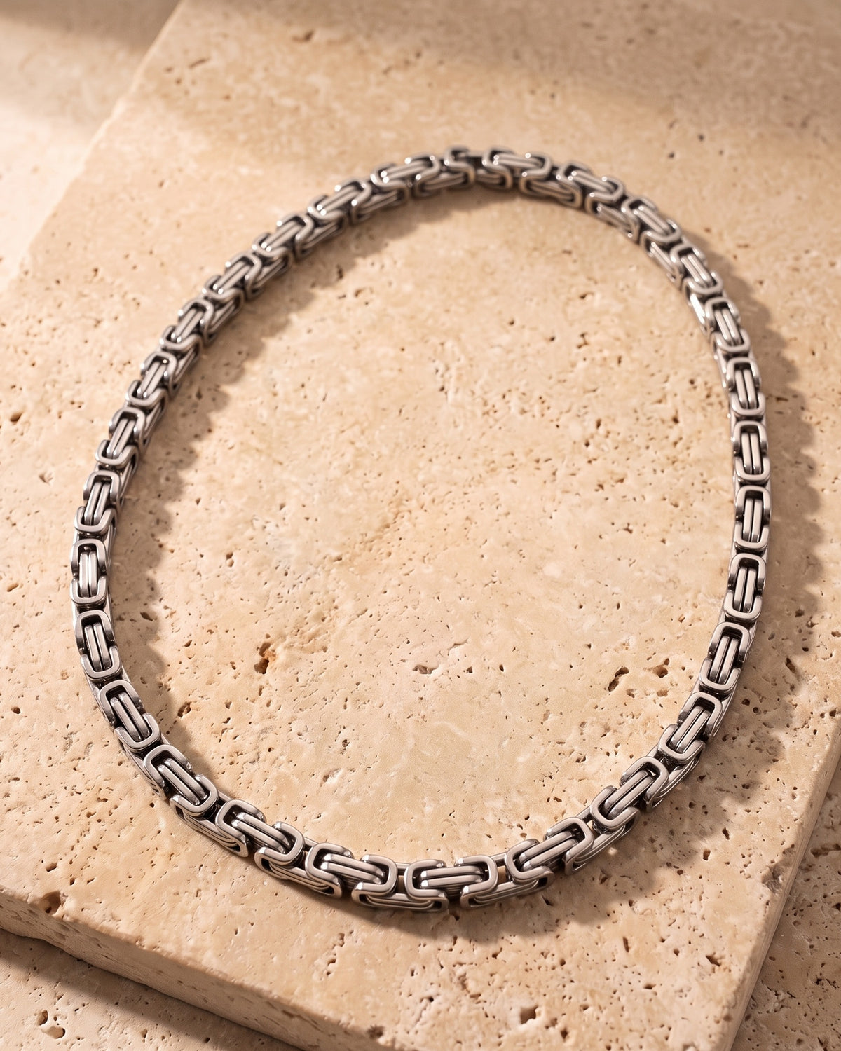The whole silver-tone Atlas Byzantine chain laid on warm stone, lobster clasp closed
