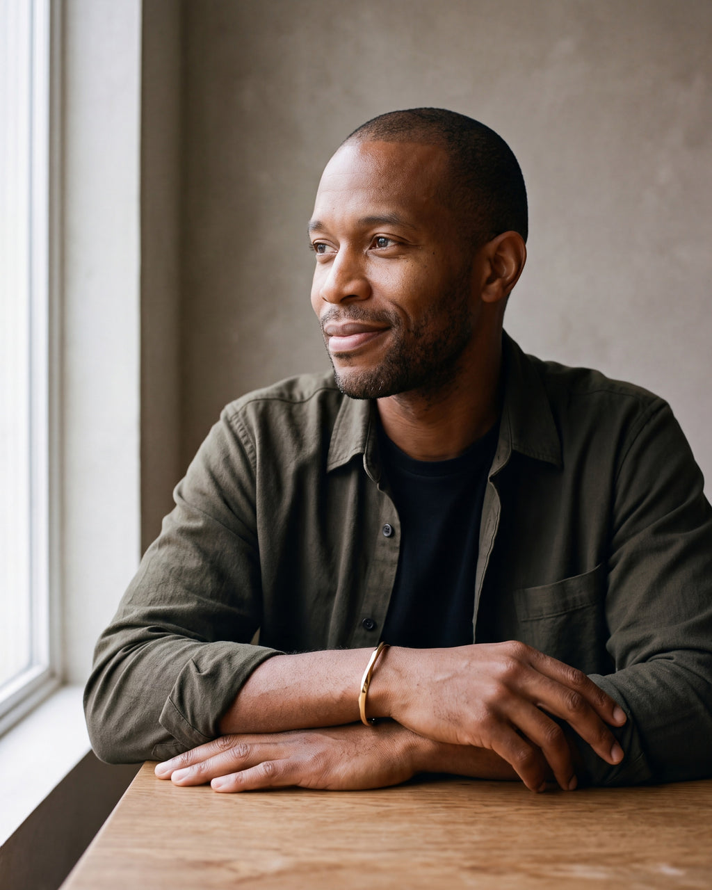 Man in a dark olive overshirt open over a black t-shirt wearing the gold-tone Atlas C-Shaped Cuff Bracelet