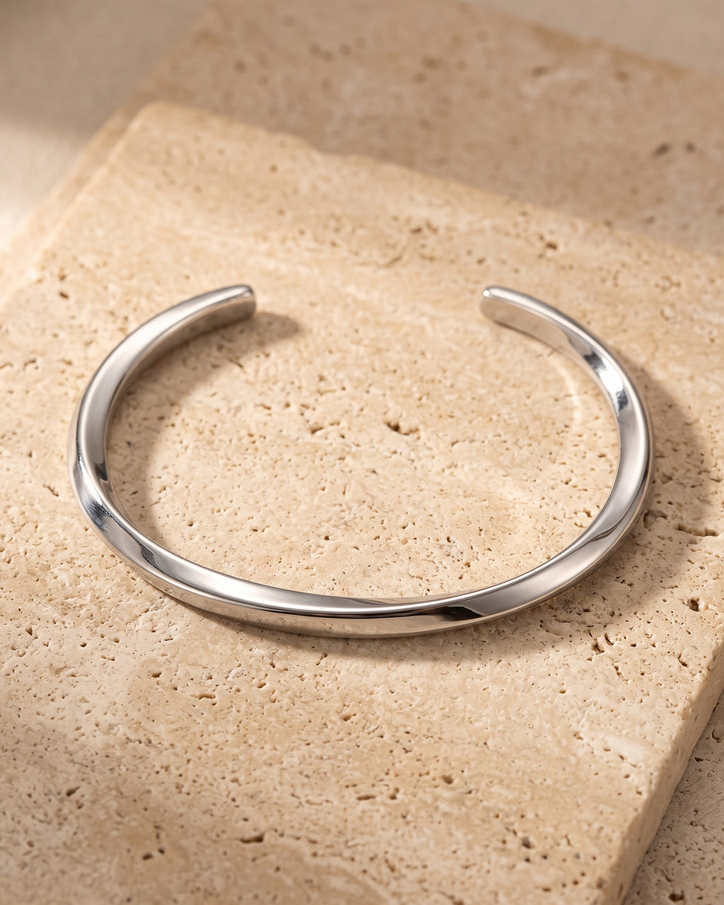 The whole silver-tone Atlas C-Shaped Cuff Bracelet lying on warm travertine stone