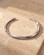 The whole silver-tone Atlas C-Shaped Cuff Bracelet lying on warm travertine stone