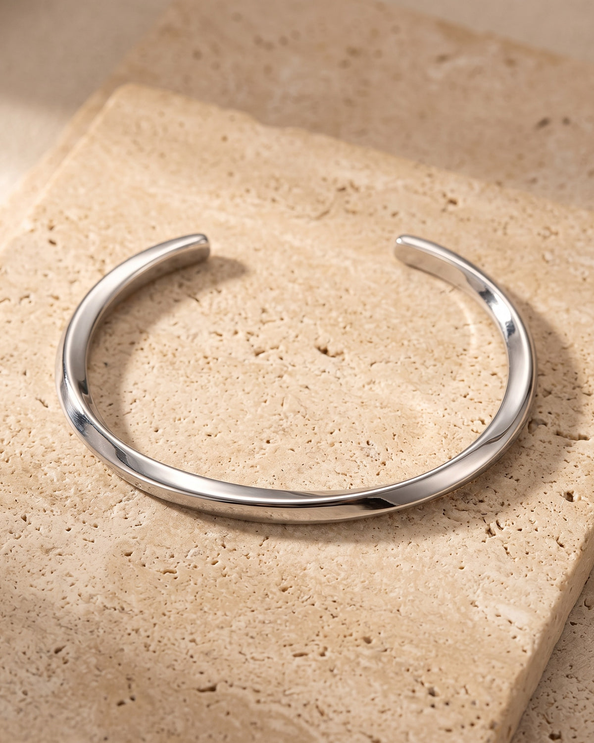 The whole silver-tone Atlas C-Shaped Cuff Bracelet lying on warm travertine stone