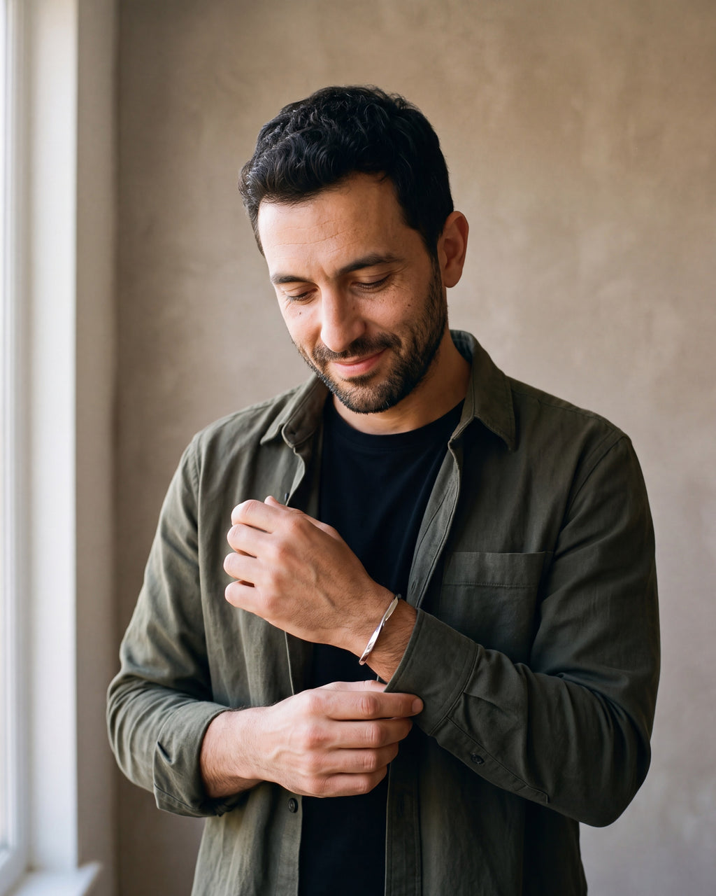 Man in a dark olive overshirt open over a black t-shirt by a window wearing the silver-tone Atlas C-Shaped Cuff Bracelet