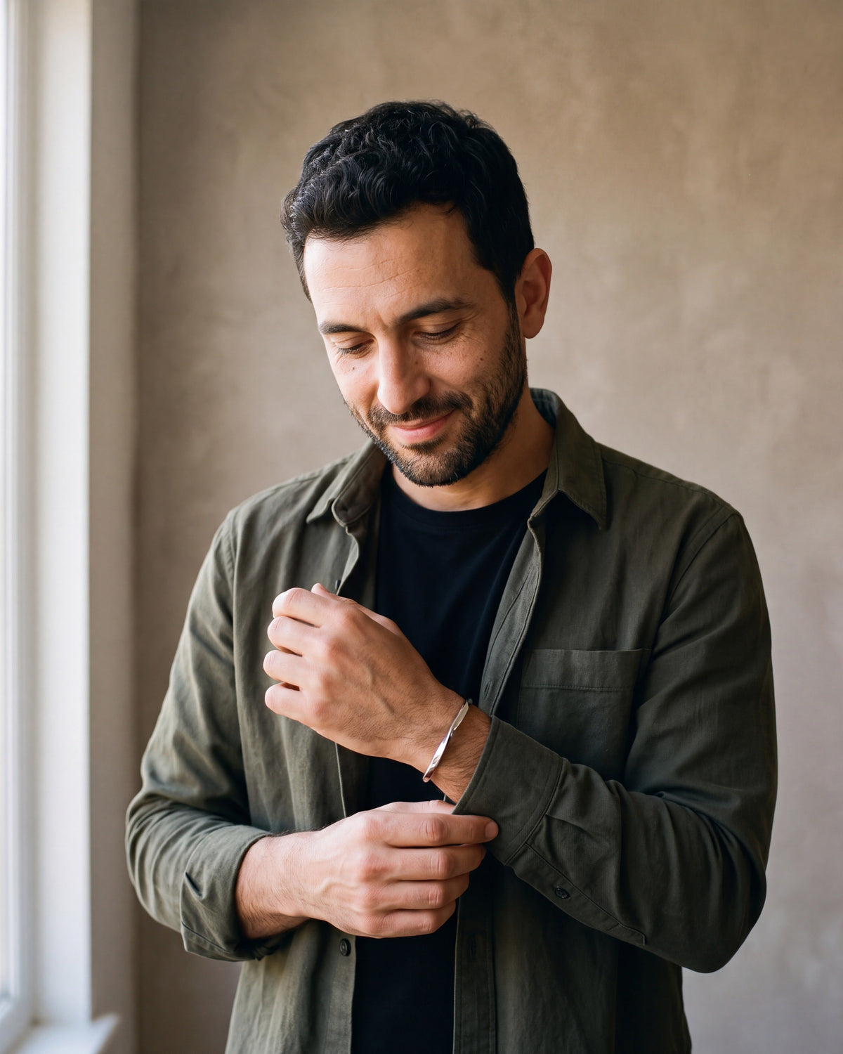 Man in a dark olive overshirt open over a black t-shirt by a window wearing the silver-tone Atlas C-Shaped Cuff Bracelet