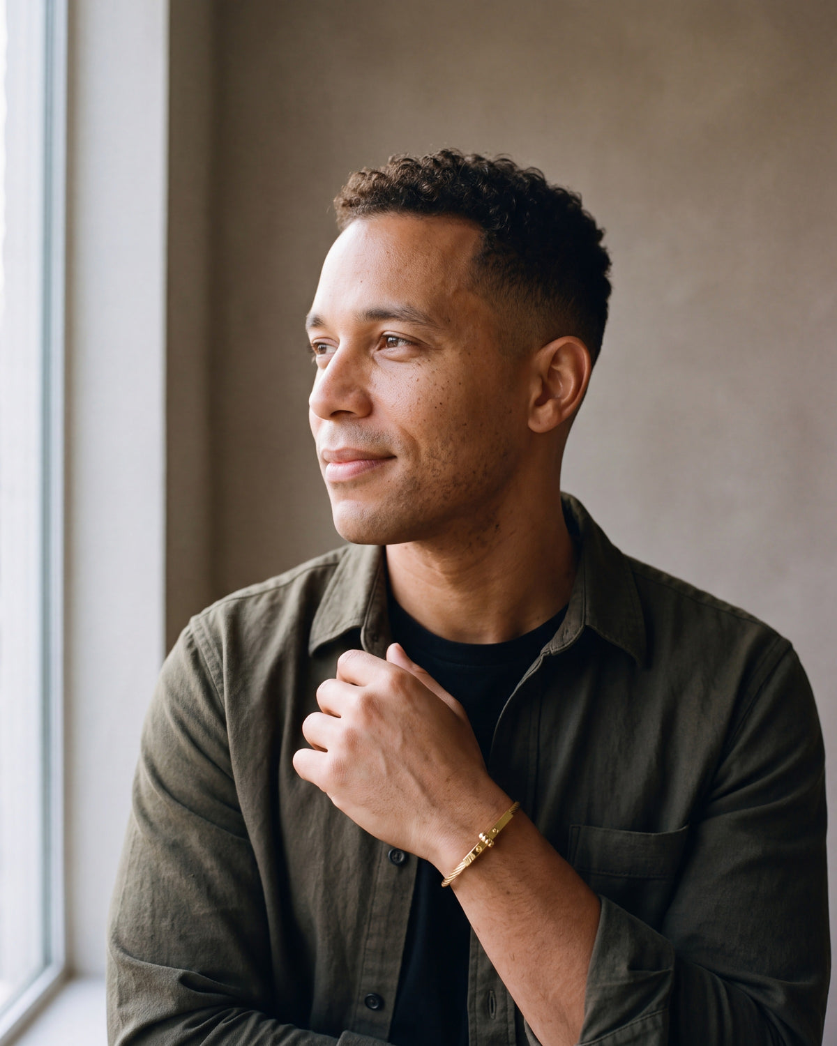 Second man in a dark olive overshirt open over a plain black t-shirt wearing the gold-tone Atlas cable bar bracelet