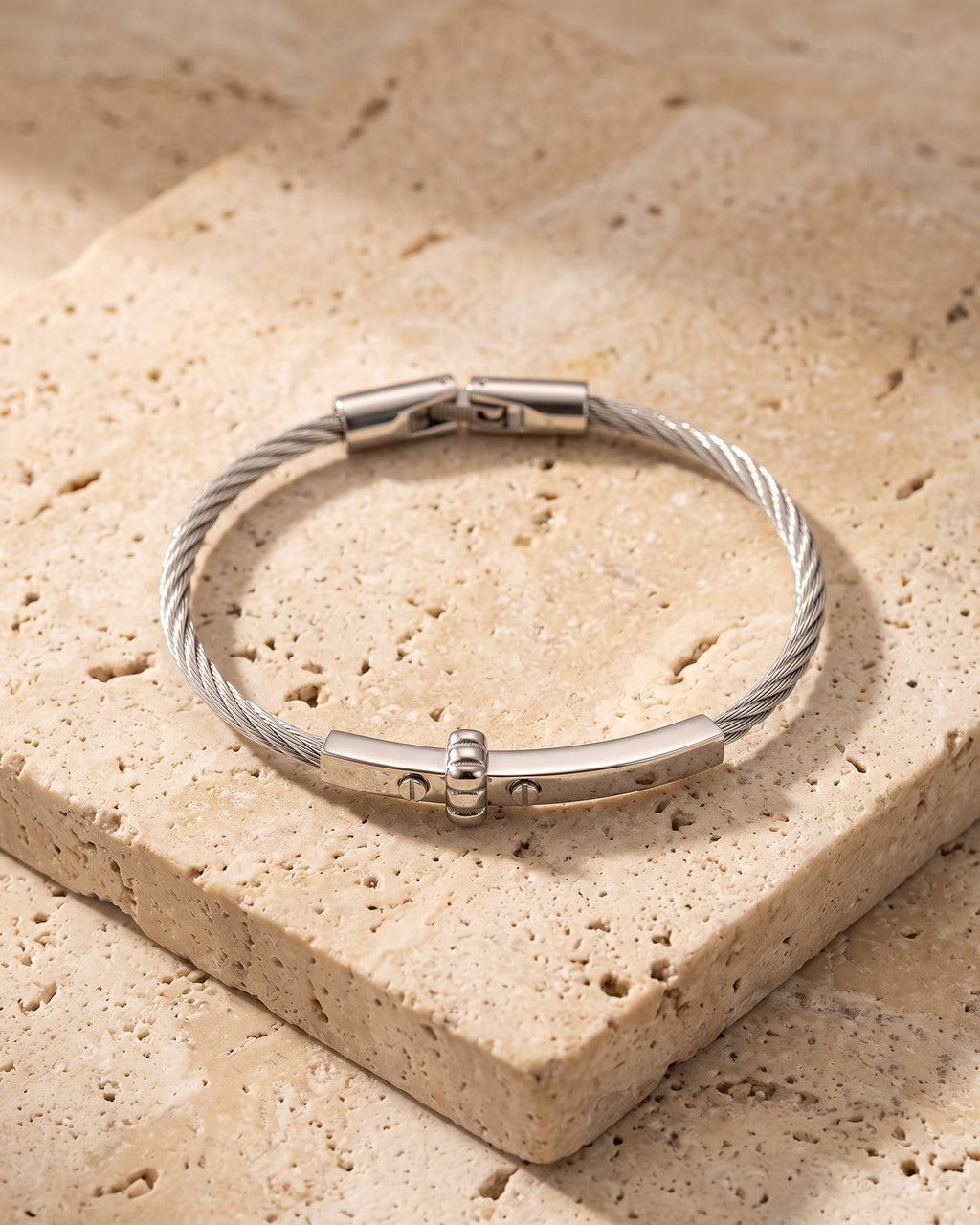 The whole silver Atlas cable bar bracelet lying on warm travertine stone