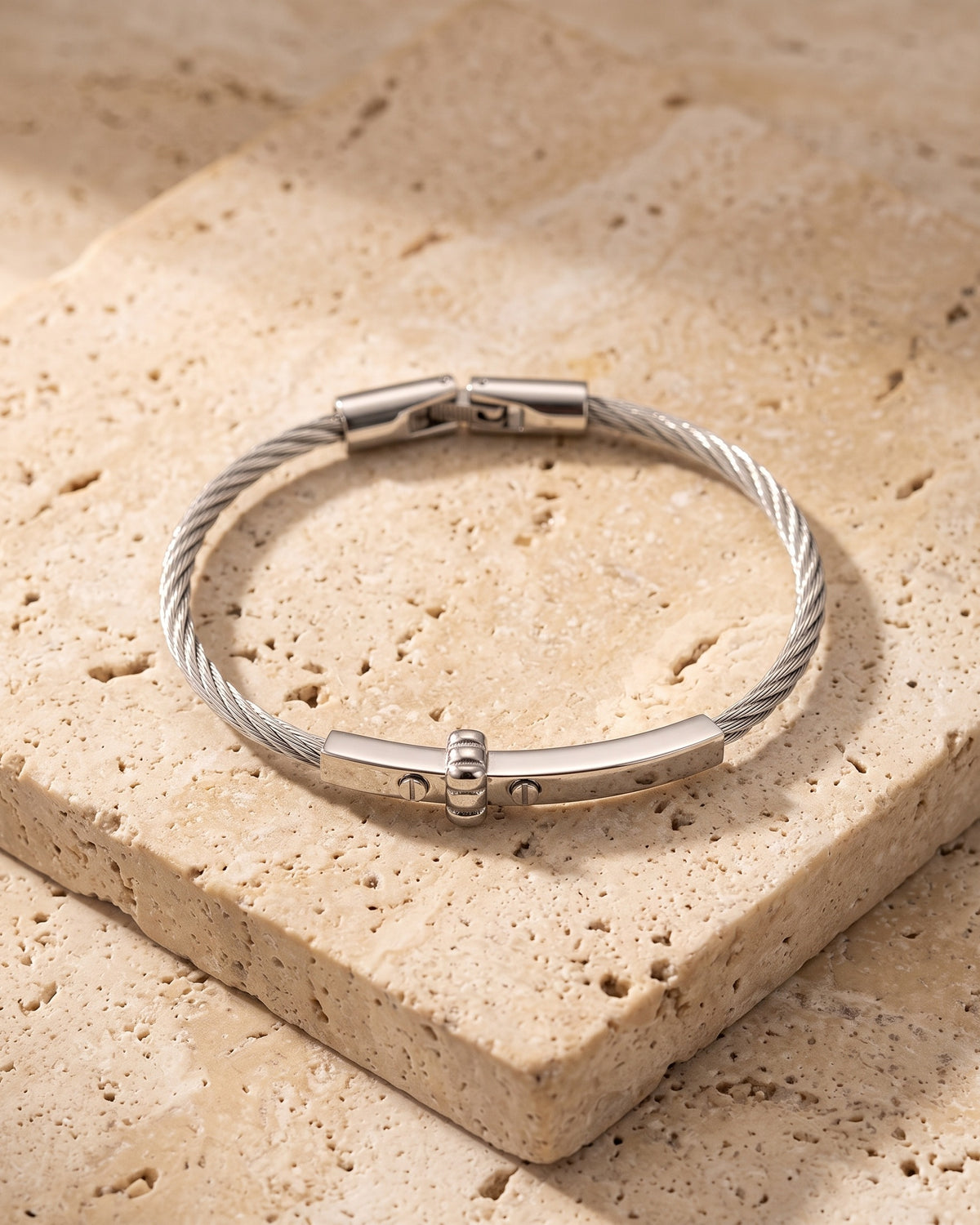 The whole silver Atlas cable bar bracelet lying on warm travertine stone