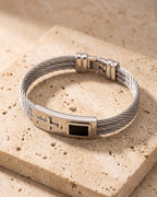 Silver Atlas cable cross bracelet closed on warm stone