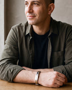 Man in an olive overshirt seated at a table, wearing the gold-tone Atlas cable cross bracelet