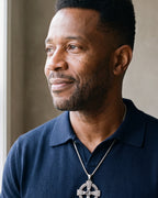 Man in a navy knit polo looking toward the window, wearing the Atlas Celtic knotwork cross pendant