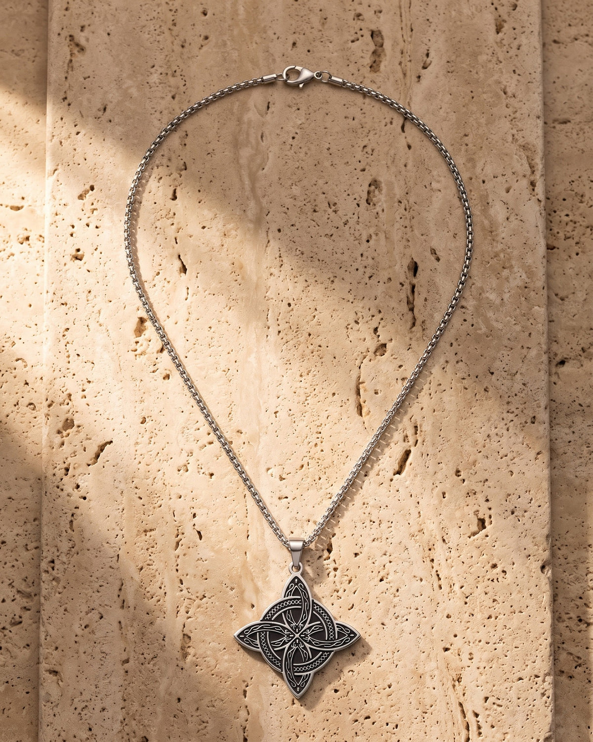 The silver Atlas Celtic Knot Necklace laid on warm travertine stone