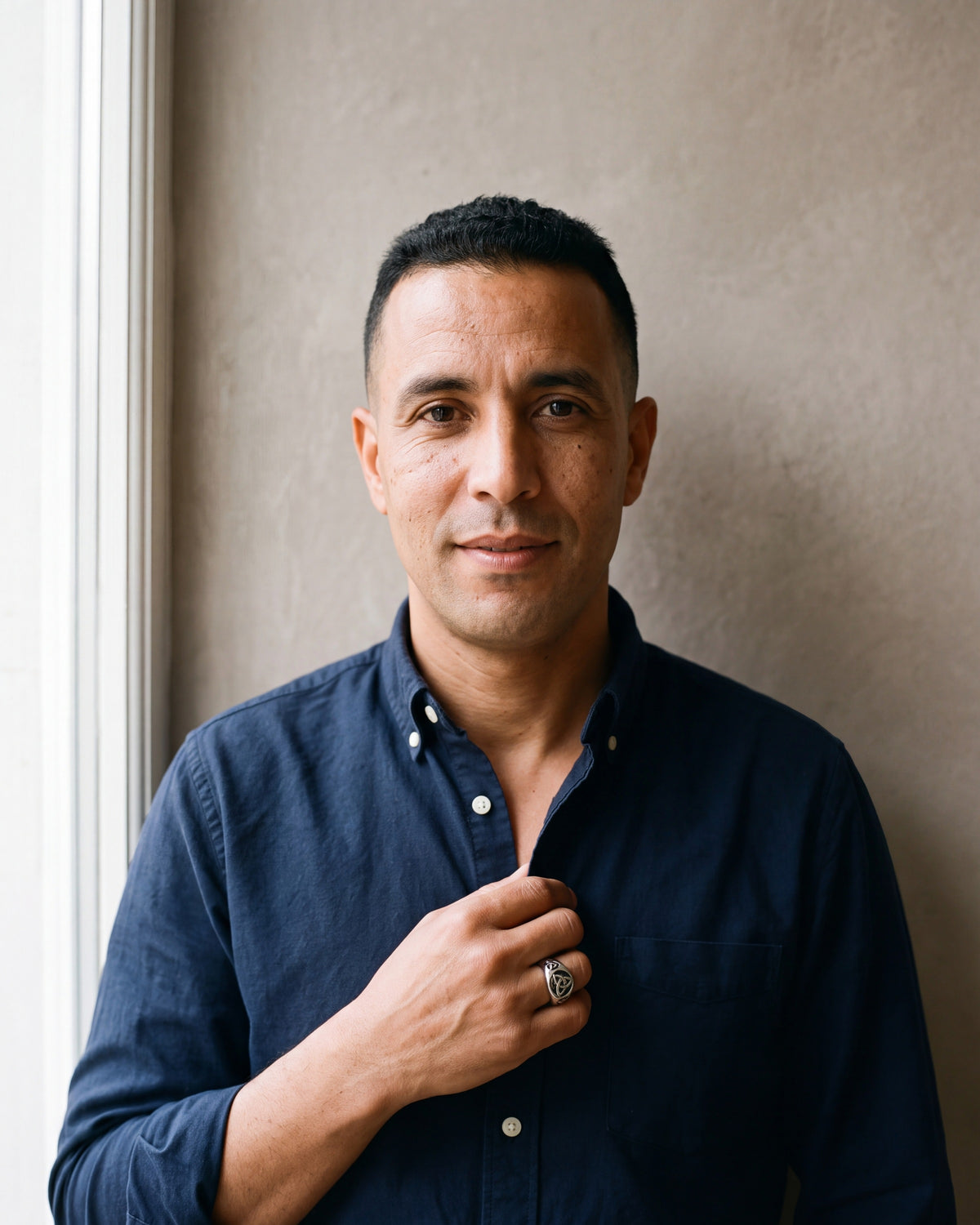 Man in a dark navy cotton oxford shirt worn open at the collar (two buttons open) by a window wearing the silver-tone Atlas celtic knot ring