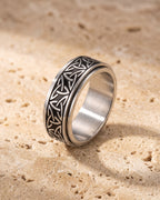 Silver Atlas Celtic knot spinner ring standing on warm stone, the knot band around its core