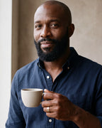 Man in a navy shirt holding a coffee cup, wearing the gold-tone Atlas Celtic knot spinner ring