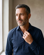 Smiling man in a navy shirt by a window wearing the silver Atlas cubic zirconia band ring on his ring finger