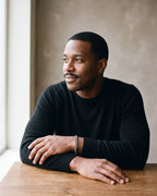 Man in a black merino sweater seated at a wooden table wearing the silver-tone Atlas classic Cuban link bracelet