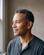 Man in a charcoal henley by a window wearing a gold-tone Atlas classic hoop earring
