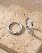 The pair of silver-tone Atlas classic hoop earrings on warm stone