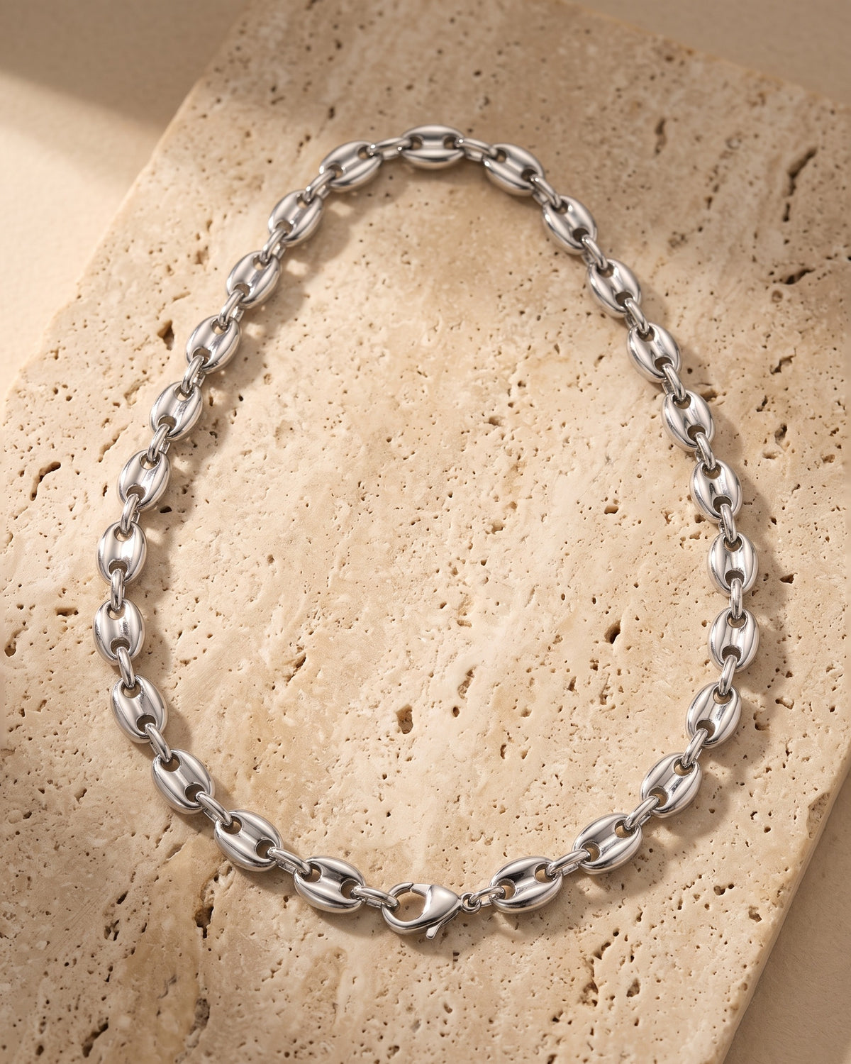 The whole silver Atlas Coffee Bean Chain lying on warm travertine stone
