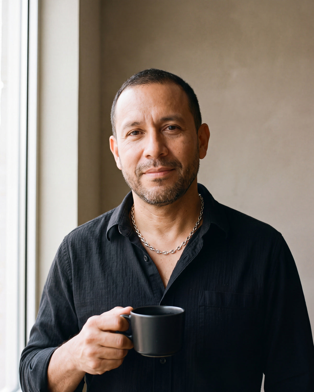 Man in a black fine cotton shirt by a window wearing the silver Atlas Coffee Bean Chain