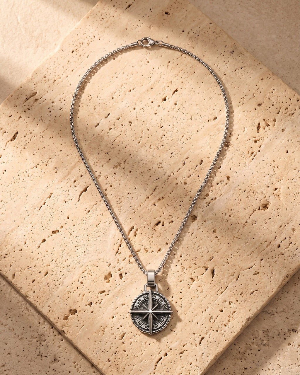 The silver Atlas Compass Pendant Necklace in Steel laid on warm travertine stone