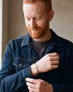 Man in a denim jacket adjusting his cuff, wearing the silver Atlas cross cuff bracelet