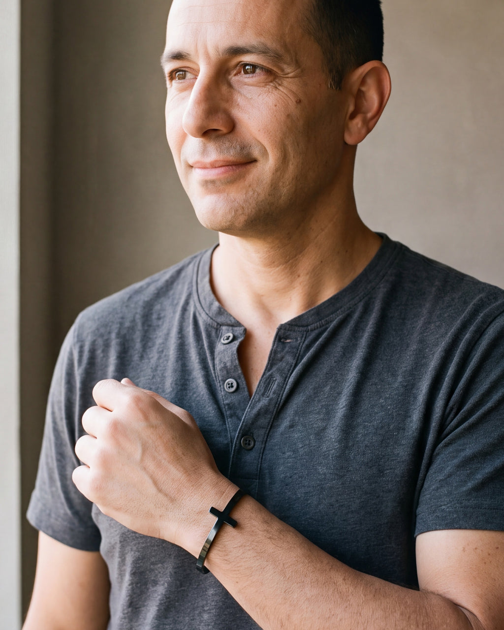 Man in a charcoal henley looking toward the window, wearing the black Atlas cross cuff bracelet