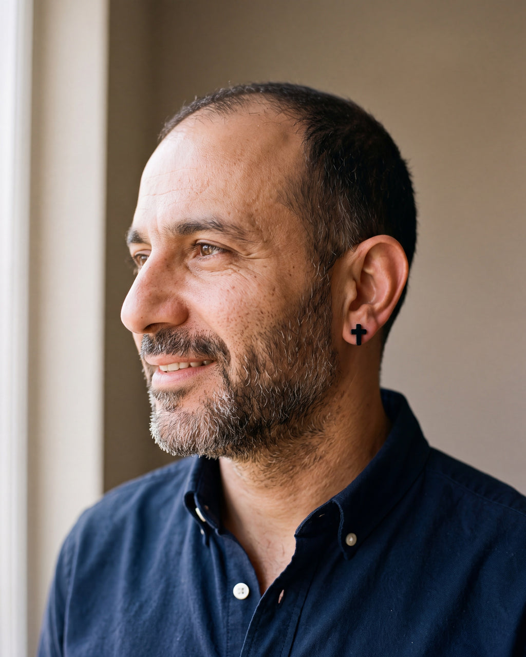 Man in a navy oxford shirt wearing the Atlas cross stud earrings in black steel