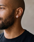 Close-up of the Atlas cross stud earrings in silver-tone steel, worn at true size