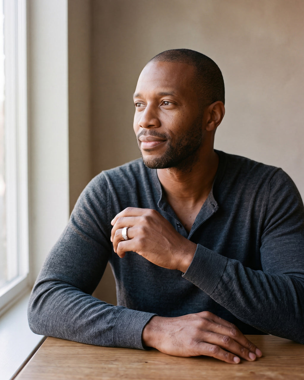Man in a fine-gauge charcoal-grey merino knit with a henley neckline by a window wearing the silver-tone Atlas Crosshatch Inlay Dome Ring