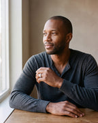Man in a fine-gauge charcoal-grey merino knit with a henley neckline by a window wearing the silver-tone Atlas Crosshatch Inlay Dome Ring
