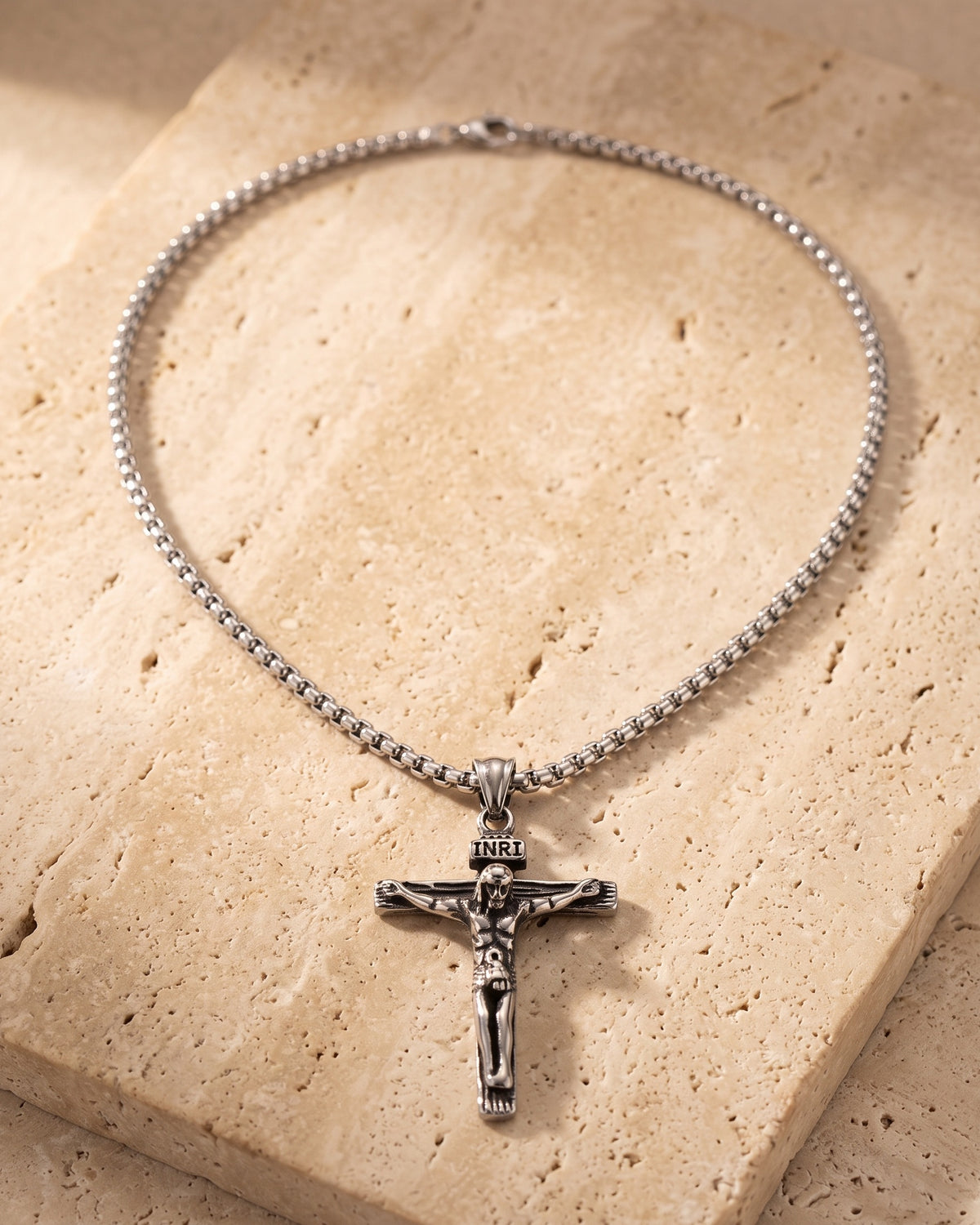 Atlas crucifix pendant and box chain laid whole on warm stone