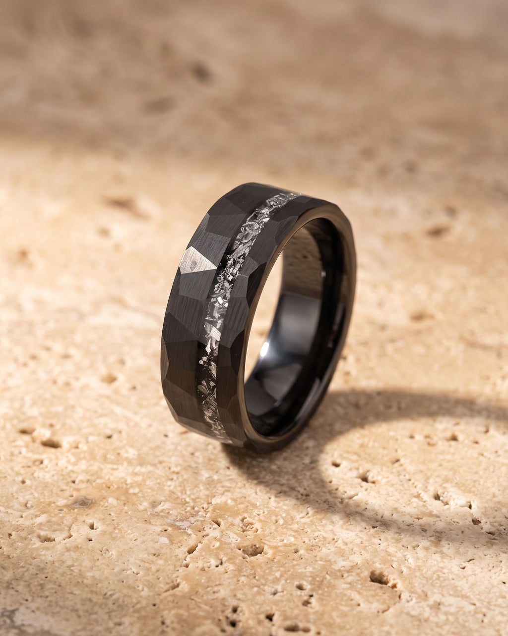 Entire Atlas crushed metal inlay ring in black steel, lying flat on warm stone