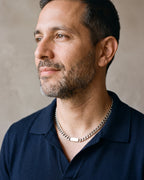 Man in a navy knit polo by a window wearing the silver Atlas Cuban bar chain