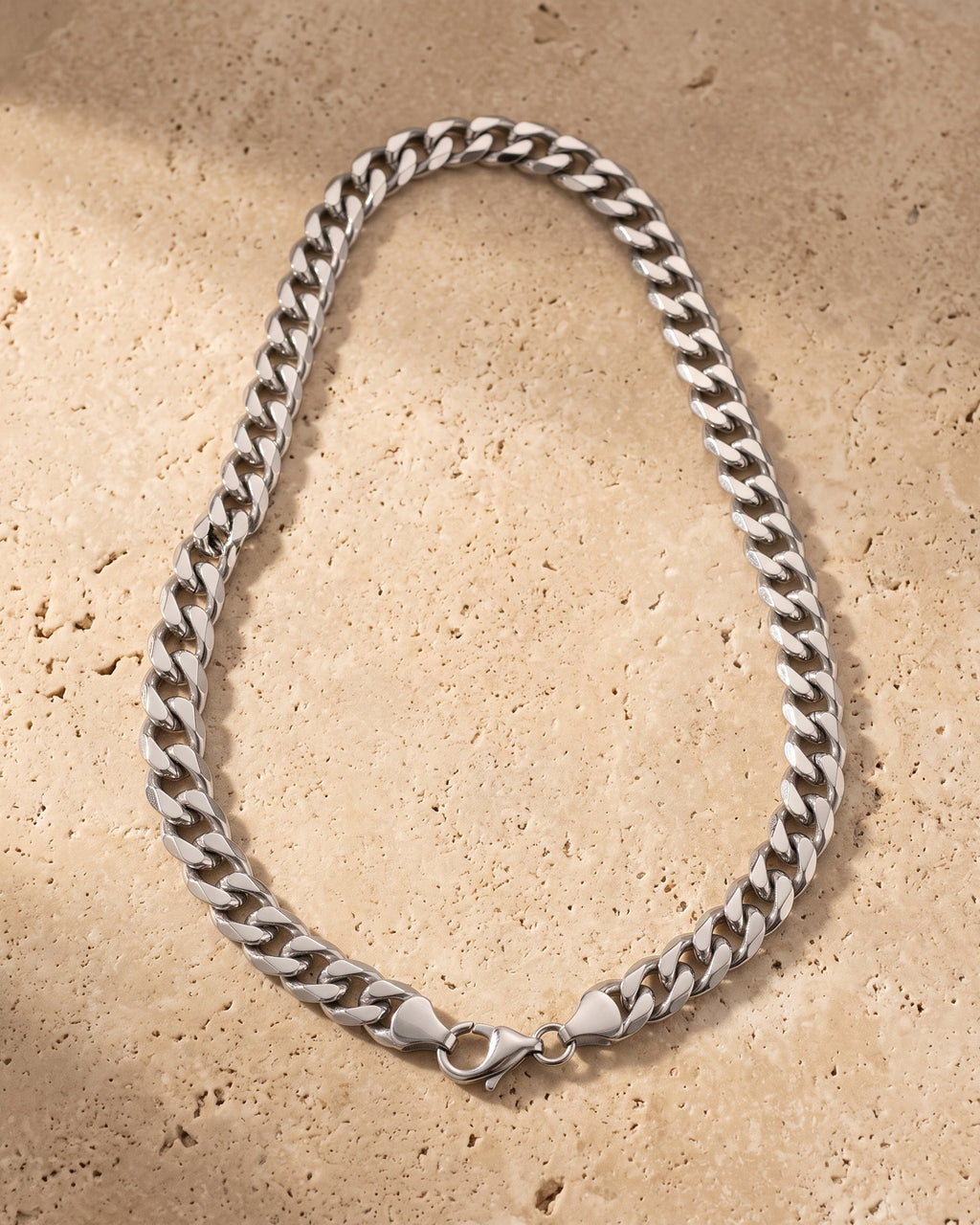 The whole silver Atlas Cuban Chain lying on warm travertine stone