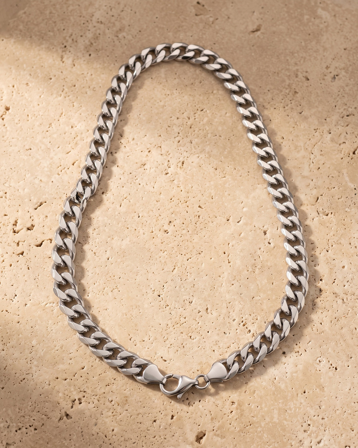 The whole silver Atlas Cuban Chain lying on warm travertine stone