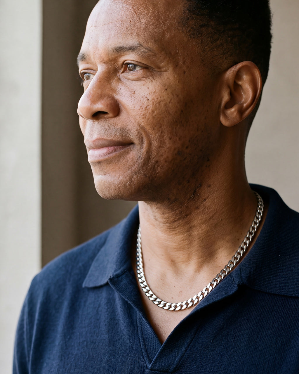 Man in a navy knit polo looking toward the window, wearing the 7 mm Atlas Cuban chain