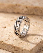 Entire Atlas Cuban link band ring in silver-tone steel, lying flat on warm stone