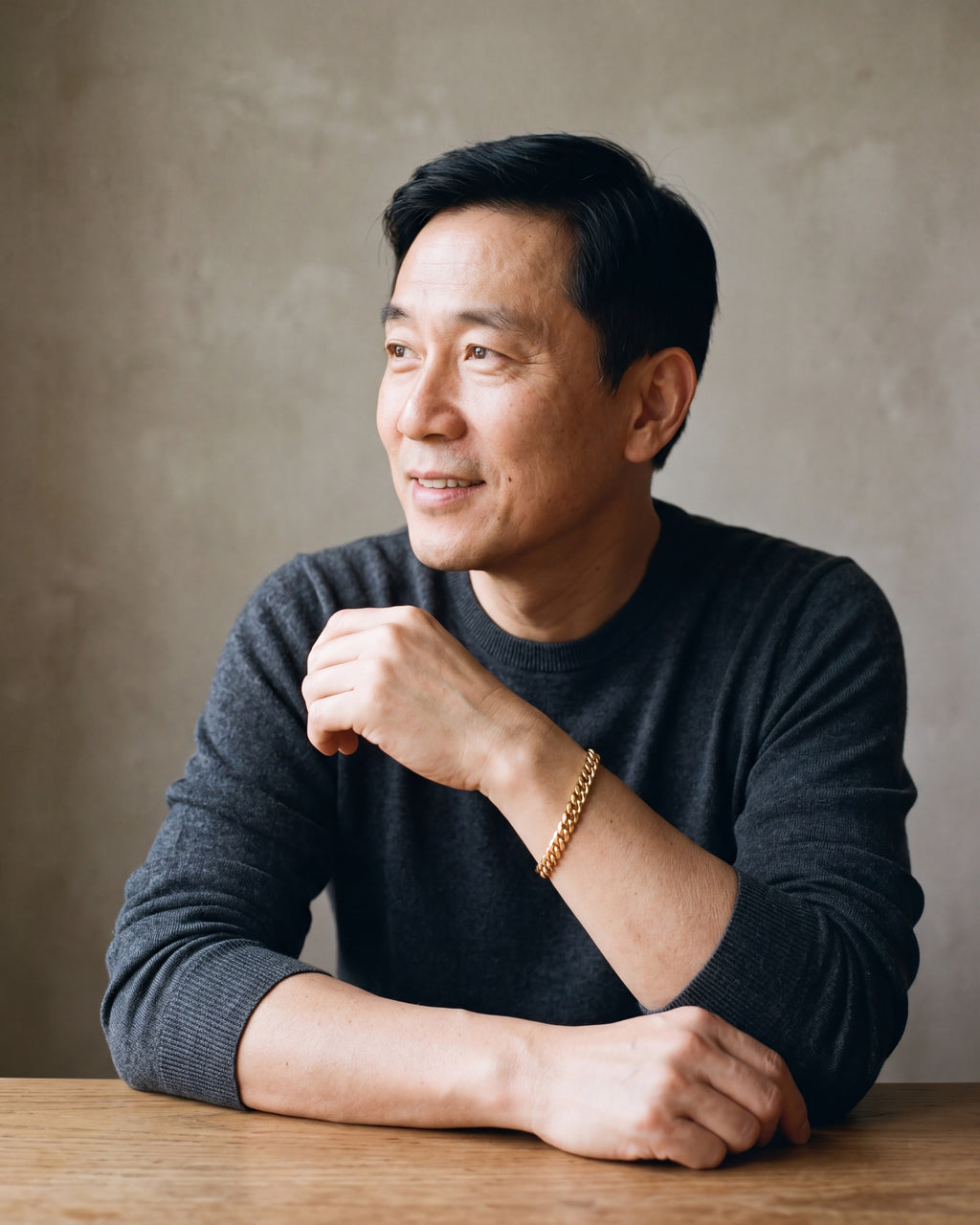 Man in a charcoal knit sweater wearing the Atlas Cuban link bracelet in gold-tone steel