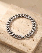 Entire Atlas Cuban link bracelet in silver-tone steel, lying flat on warm stone