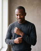 Man in a charcoal knit sweater by a window wearing the Atlas Cuban link bracelet in silver-tone steel