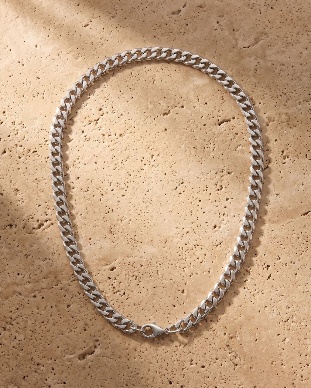 The silver Atlas Cuban Link Chain in Stainless Steel laid on warm travertine stone