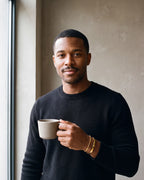 Man in a black merino sweater holding a coffee cup wearing the gold-tone Atlas cuff and chain bracelet set