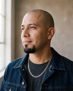 Man in a denim jacket over a charcoal t-shirt by a window wearing the Atlas curb chain in silver-tone steel