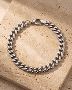 Entire Atlas curb link bracelet in silver-tone steel, lying flat on warm stone