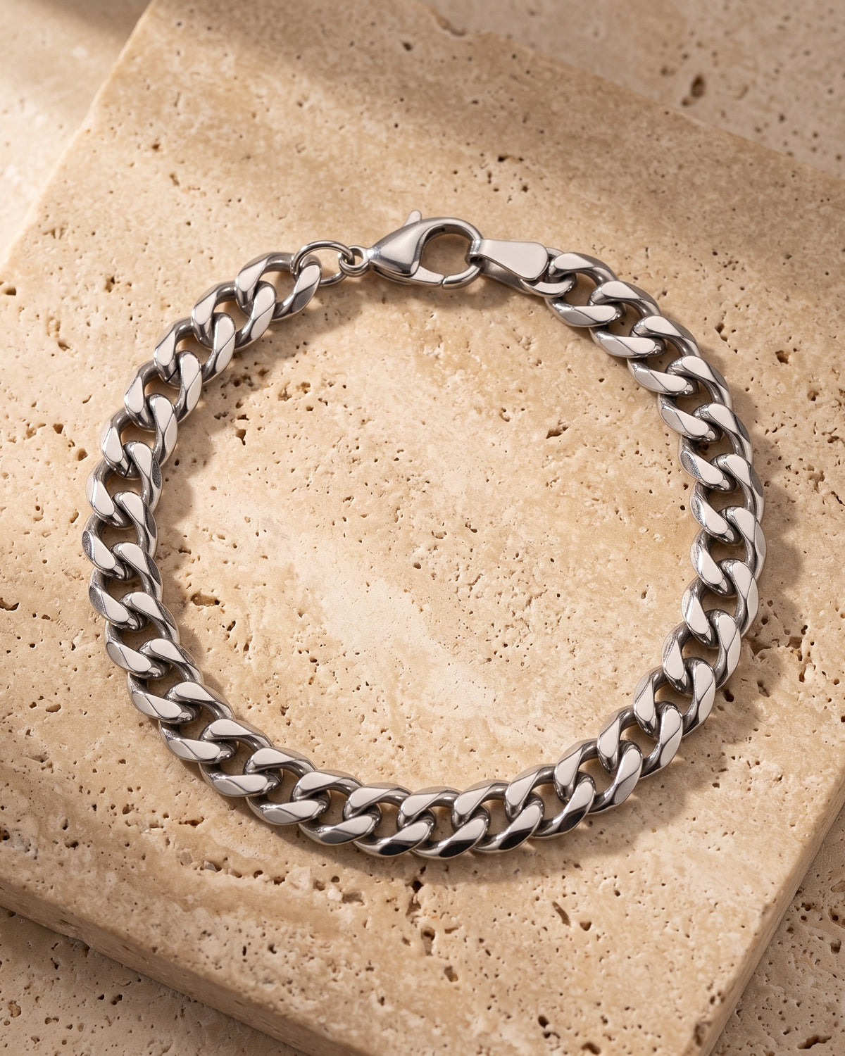 Entire Atlas curb link bracelet in silver-tone steel, lying flat on warm stone