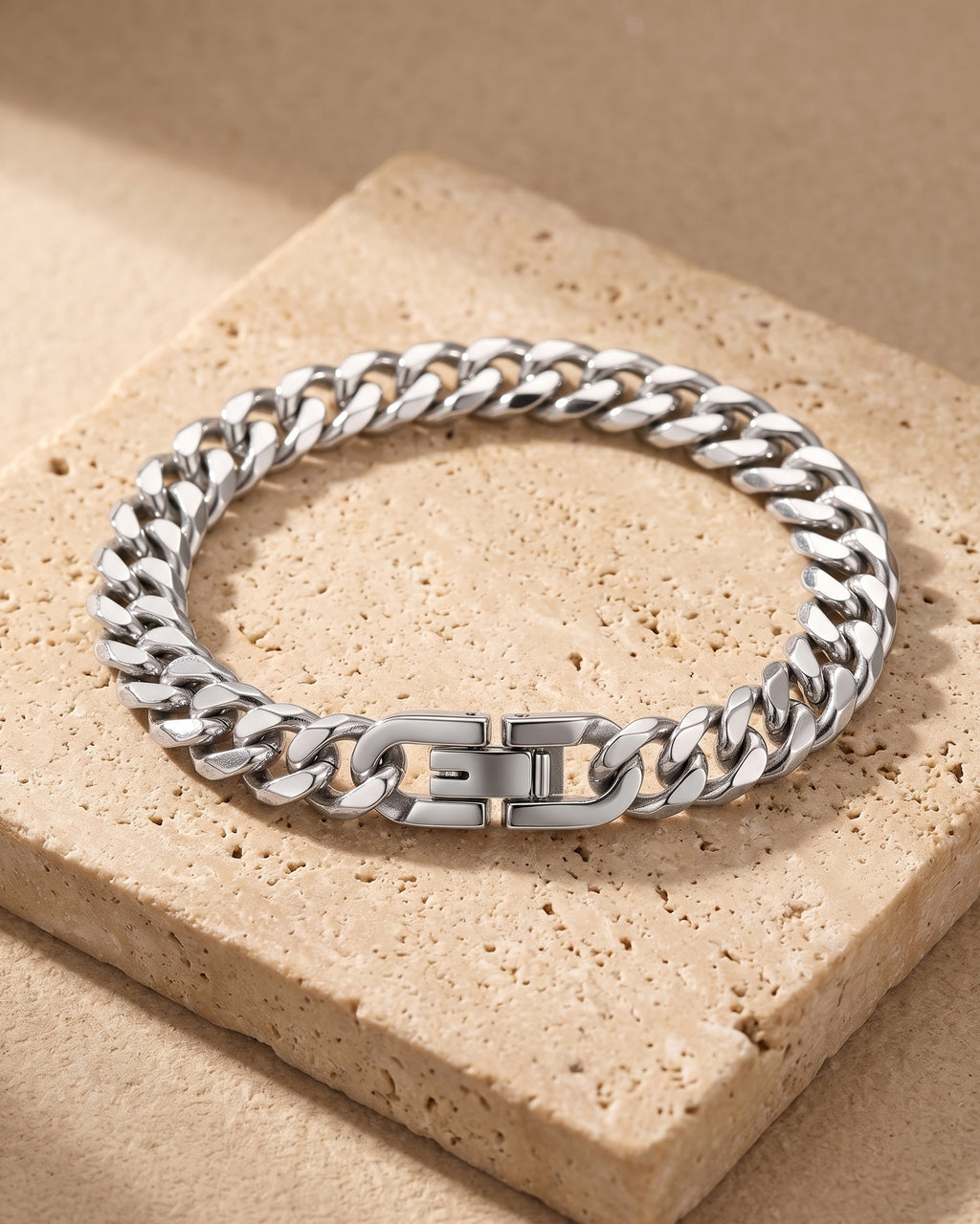 Entire Atlas curb link bracelet in silver-tone steel, lying flat on warm stone