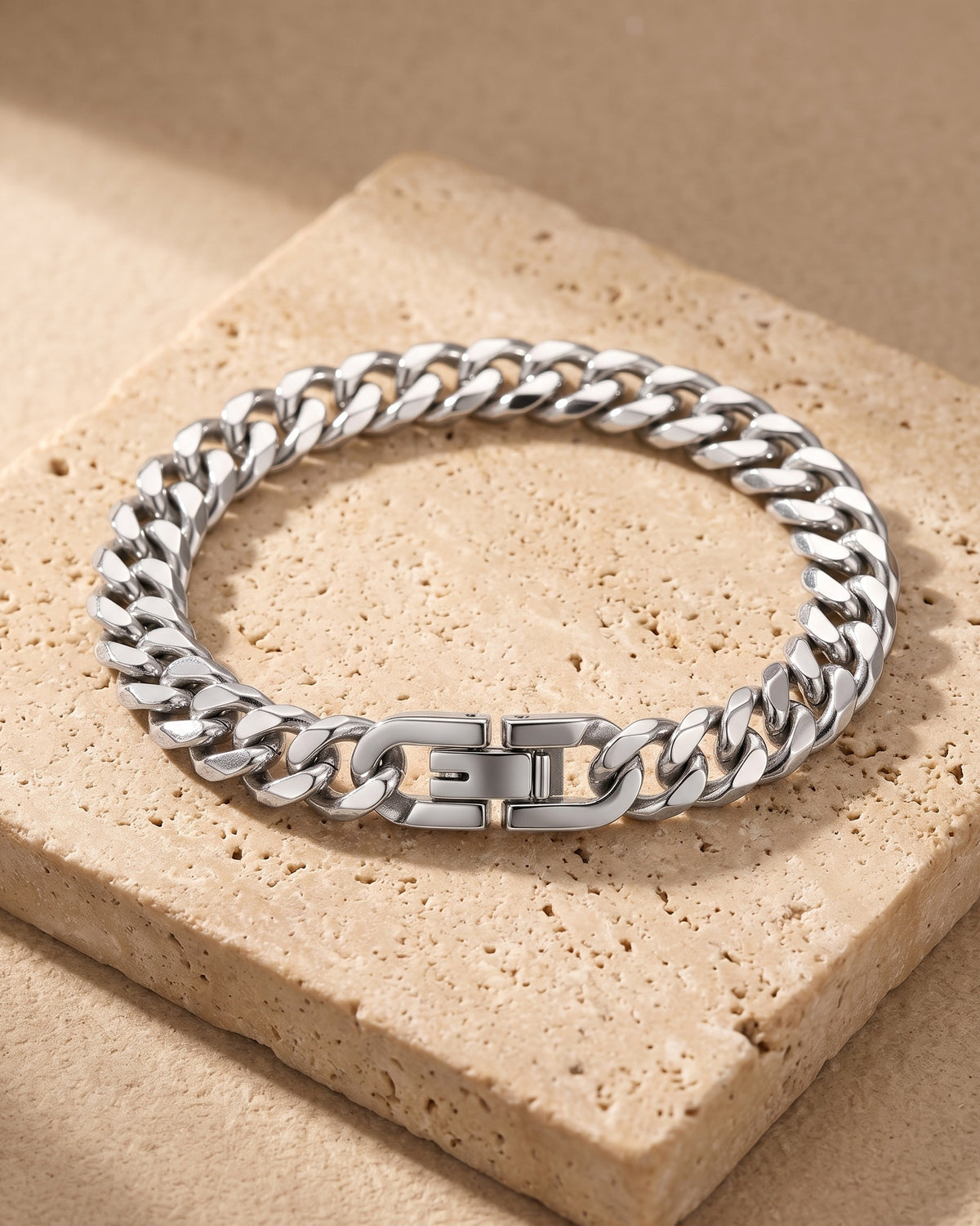 Entire Atlas curb link bracelet in silver-tone steel, lying flat on warm stone